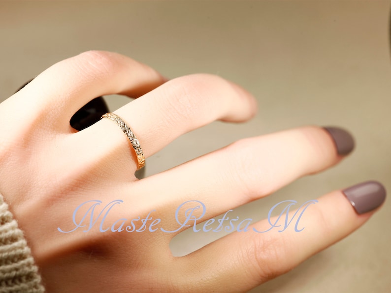 Puede incluir: Un fino anillo de banda de oro con un dise&ntilde;o texturizado. El anillo se lleva en un dedo con esmalte de u&ntilde;as marr&oacute;n claro.