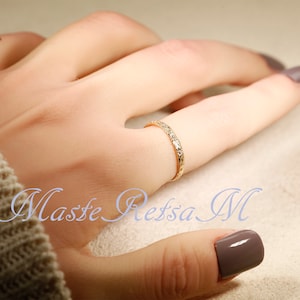 Puede incluir: Un delicado anillo de banda de oro con una superficie texturizada. El anillo se lleva en un dedo con un esmalte de u&ntilde;as marr&oacute;n claro.