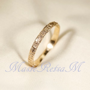 May include: A thin gold band ring with a floral design engraved around the entire band.