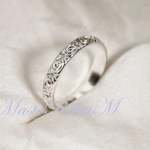 Puede incluir: Un anillo de plata con un intrincado dise&ntilde;o floral. El dise&ntilde;o del anillo presenta motivos circulares y florales repetidos, creando una superficie texturizada. El anillo se muestra sobre una tela blanca texturizada.