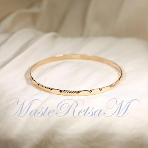 May include: A gold bangle bracelet with a textured design. The bracelet is on a white fabric background.