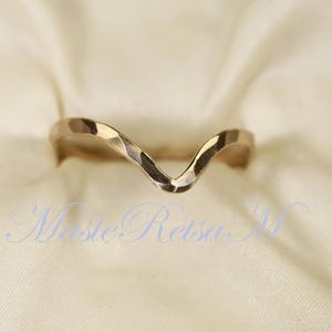 May include: A gold-toned ring with a wavy, V-shaped design. The ring is made of metal and has a hammered texture.