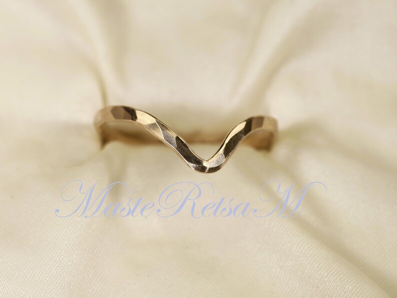 May include: A gold-toned ring with a wavy, V-shaped design. The ring is made of metal and has a hammered texture.