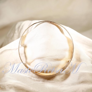 May include: A gold-toned bangle bracelet on a white fabric background.