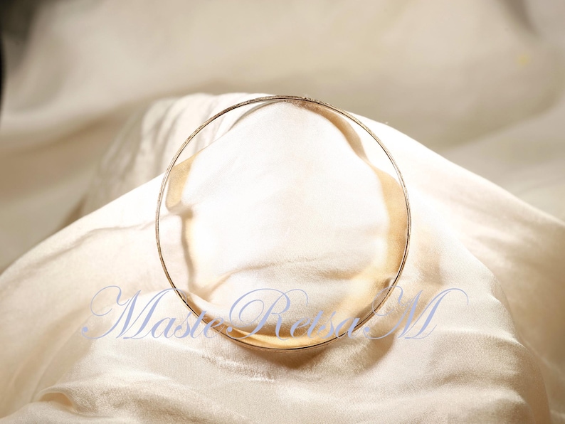 May include: A gold-toned bangle bracelet on a white fabric background.