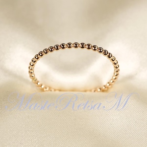 Pode incluir: Um delicado anel de ouro com um design de contas. O anel é feito de pequenas contas redondas que são igualmente espaçadas ao longo da banda.