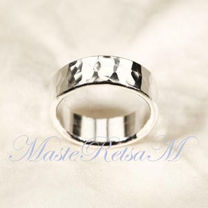 May include: A silver ring with a hammered texture. The ring has a wide band and a polished interior. The ring is displayed on a white fabric background. The text "MasteRetsa M" is visible in the image.