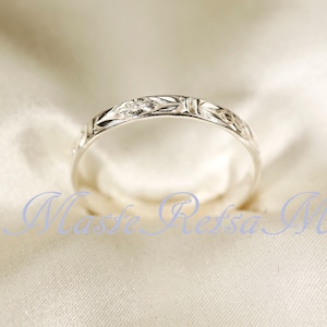 May include: A silver ring with a floral and geometric pattern. The ring is thin and has a polished finish. The design features small flowers and other decorative elements. The ring is displayed on a white satin surface.