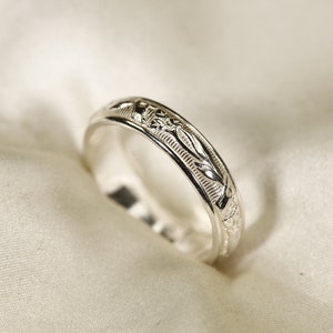 Può includere: Una fede nuziale in argento con un intricato design floreale.