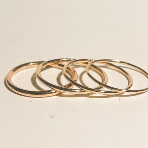 May include: Four gold-coloured stacking rings, each with a smooth, rounded surface. The rings are arranged in a graduated size order, with the largest ring at the bottom and the smallest ring at the top.