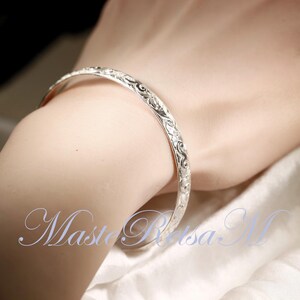 May include: A silver bangle bracelet with an intricate floral design.