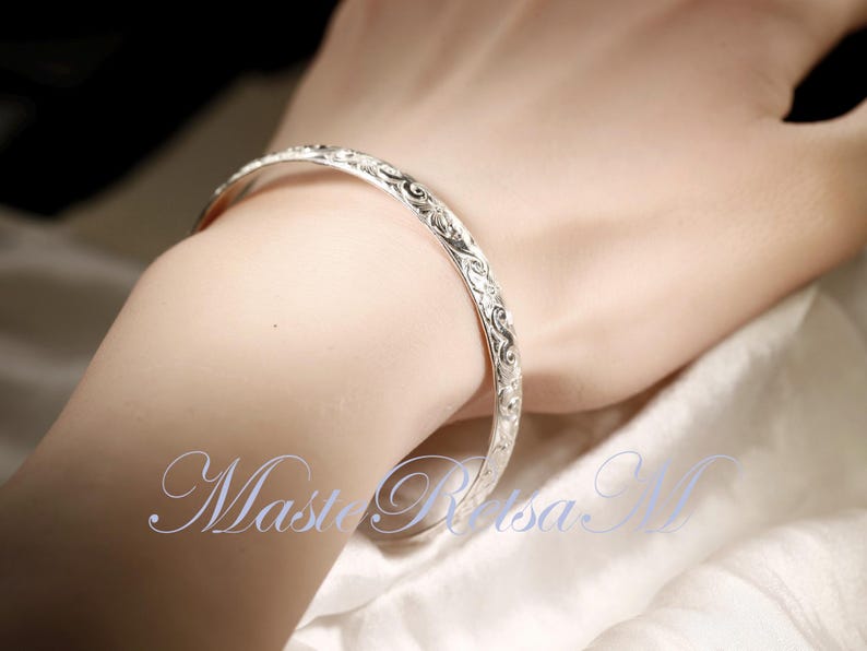 May include: A silver bangle bracelet with an intricate floral design.