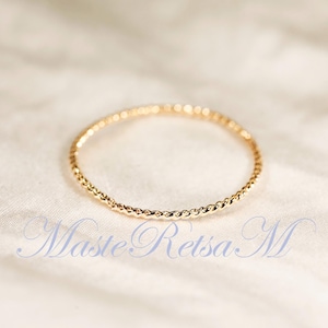 May include: A thin, gold-coloured ring with a twisted, rope-like texture throughout the entire band. The ring is circular and features a polished, reflective surface. The text MasteRetsaM is visible in a blue, cursive font at the bottom of the image.