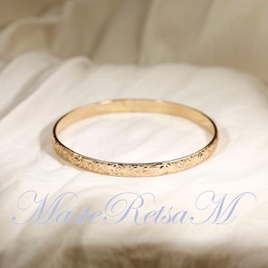 May include: A gold bangle bracelet with an intricate floral design.