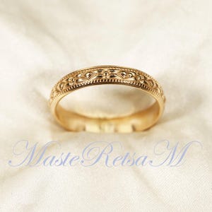 Könnte beinhalten: Ein goldener Ehering mit einem zarten floralen Design.