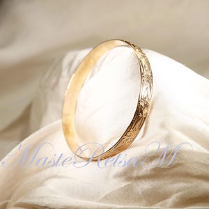 May include: A gold bangle bracelet with an intricate floral design. The bracelet is smooth and shiny, and the floral pattern is raised and detailed.