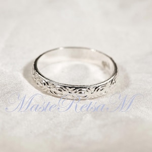 Puede incluir: Un anillo de plata con un patr&oacute;n circular repetido alrededor de la banda. El anillo est&aacute; sobre un fondo blanco texturizado. Es una pieza de joyer&iacute;a.