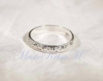 May include: A silver ring with a repeating circular pattern around the band. The ring is set against a white, textured background. The ring is a piece of jewellery.