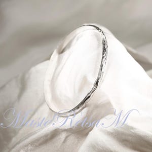 May include: A silver bangle bracelet with a textured, twisted design. The bracelet is on a white fabric background.
