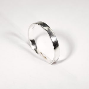 May include: A silver ring with a flat band. The ring is made of a shiny, reflective metal and is set against a white background. The ring's simple design makes it suitable for everyday wear.