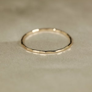 May include: A simple gold band ring with a hammered texture.