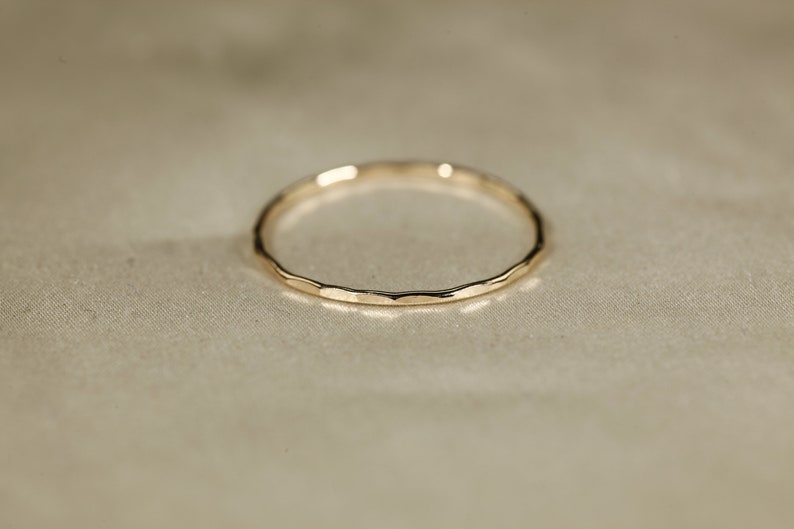 May include: A simple gold band ring with a hammered texture.