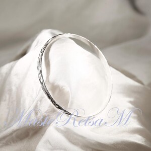 May include: A silver bangle bracelet with a textured surface.