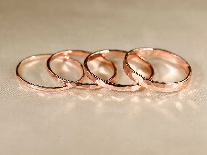 May include: Four hammered rose gold rings stacked on top of each other. The rings are all the same width and have a slightly textured surface.