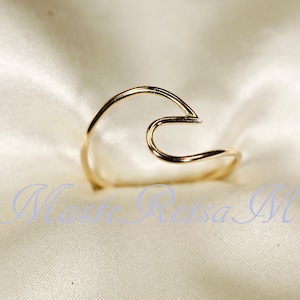 May include: Gold wave ring. The ring is made of a single piece of wire that is bent into the shape of a wave. The ring is simple and elegant.