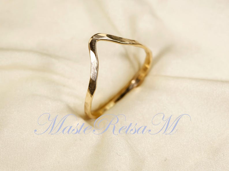 May include: A gold-toned, hammered, open ring with a V-shaped design. The ring is made of metal and has a smooth, polished finish.