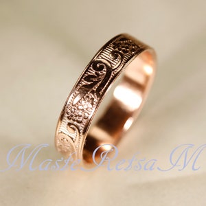 May include: A rose gold ring featuring an engraved floral pattern with swirling vines and small blossoms. The band has a polished finish and a flat profile, showcasing intricate metalwork that wraps around the entire circumference of the ring.