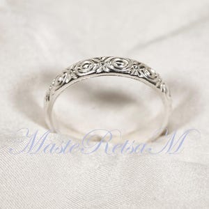 Puede incluir: Un anillo plateado con un intrincado dise&ntilde;o floral. La superficie del anillo est&aacute; adornada con un patr&oacute;n repetitivo de espirales y motivos florales. El anillo est&aacute; sobre un fondo blanco, resaltando el dise&ntilde;o detallado.