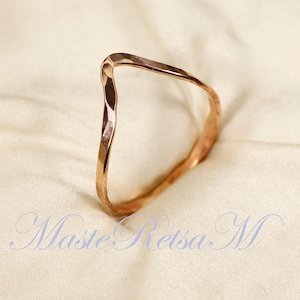 May include: A rose gold hammered metal ring with a V-shaped design.