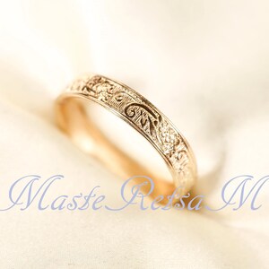May include: A gold ring featuring an intricate, embossed floral and scrollwork pattern along its outer band. The metal has a warm, polished finish, and the design consists of repeating organic shapes and fine lines engraved across the surface.