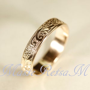 May include: A gold-toned metal ring featuring an intricate, engraved floral and scrollwork pattern along its outer band. The surface of the ring displays a repeating design of small flowers and curved leaf motifs, with a polished finish.