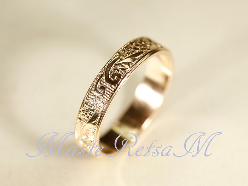 May include: A gold-toned metal ring featuring an intricate, engraved floral and scrollwork pattern along its outer band. The surface of the ring displays a repeating design of small flowers and curved leaf motifs, with a polished finish.