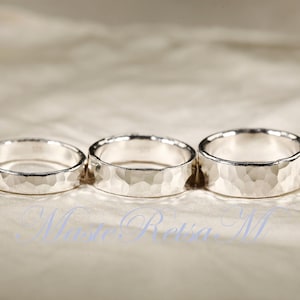 May include: Three silver rings with a hammered texture are displayed on a light-colored surface. The rings are of varying sizes, with a textured surface. The rings are likely wedding bands or fashion accessories.