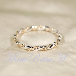 May include: A thin ring featuring a twisted design with alternating strands of polished silver and textured gold metal. The band has a continuous rope-like pattern that wraps around the entire circumference, creating a delicate and layered appearance.