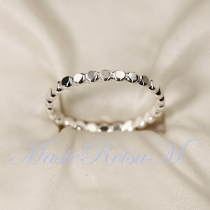 Puede incluir: Un anillo de plata con un diseño de cuentas. Las cuentas son pequeñas y redondas, y están espaciadas uniformemente alrededor del anillo.