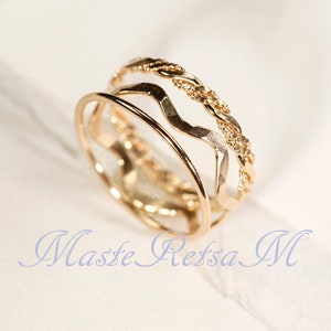 May include: Three gold rings stacked on top of each other. The top ring is a braided design, the middle ring is a wavy design, and the bottom ring is a simple band.