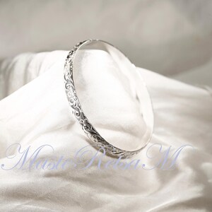 May include: A silver bangle bracelet with an intricate floral design.