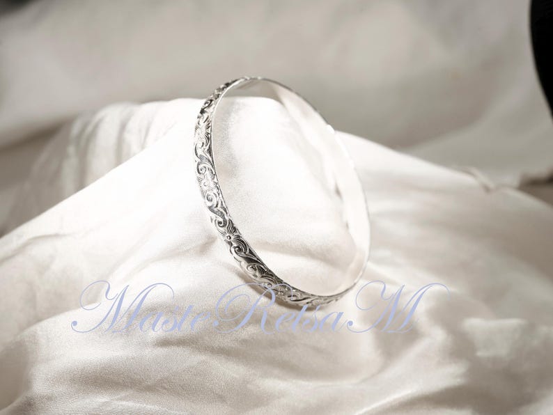 May include: A silver bangle bracelet with an intricate floral design.