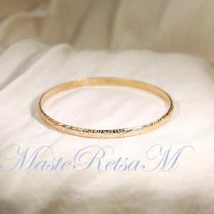May include: A gold bangle bracelet with an intricate floral design.