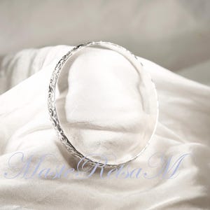 May include: A silver bangle bracelet with an intricate floral design.
