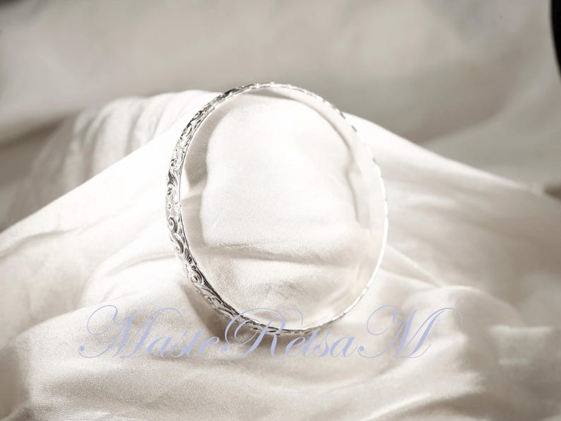 May include: A silver bangle bracelet with an intricate floral design.