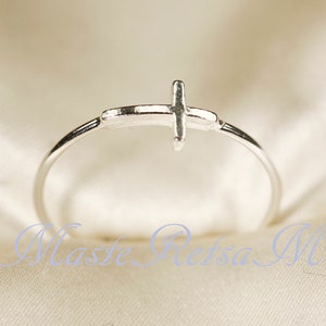 May include: A silver ring with a simple cross design.