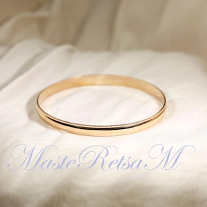 May include: A gold bangle bracelet with a smooth, rounded surface and a subtle textured edge.