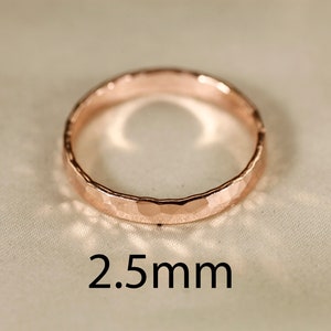 May include: A close-up of a hammered rose gold band ring. The ring is 2.5 mm wide.