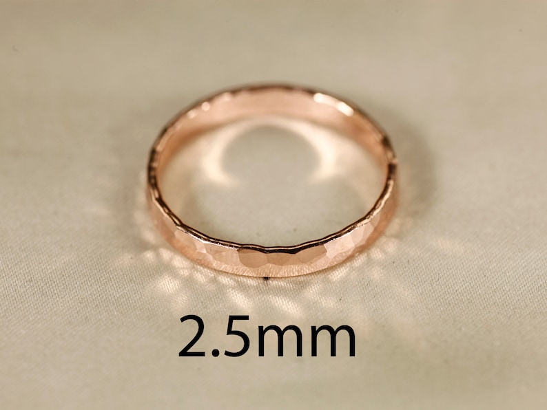May include: A close-up of a hammered rose gold band ring. The ring is 2.5 mm wide.
