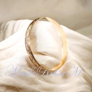 May include: A gold bangle bracelet with an intricate floral design. The bracelet is smooth and shiny.